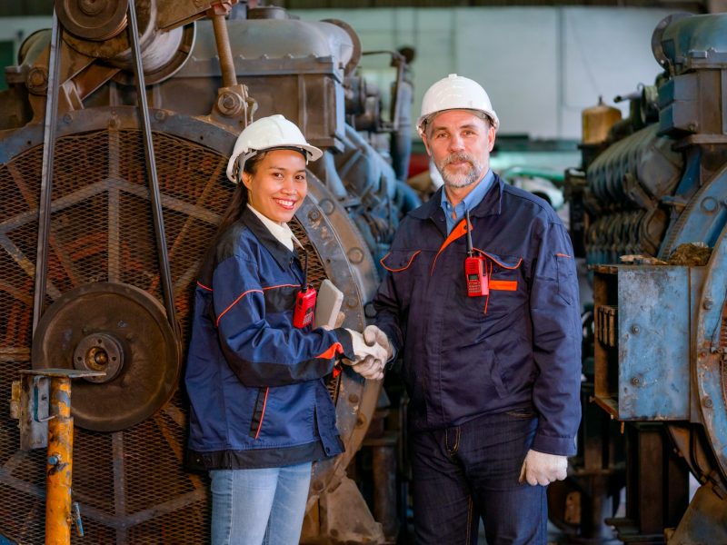 Factory worker or technician stand and shake hands with Asian factory woman in front of big machine